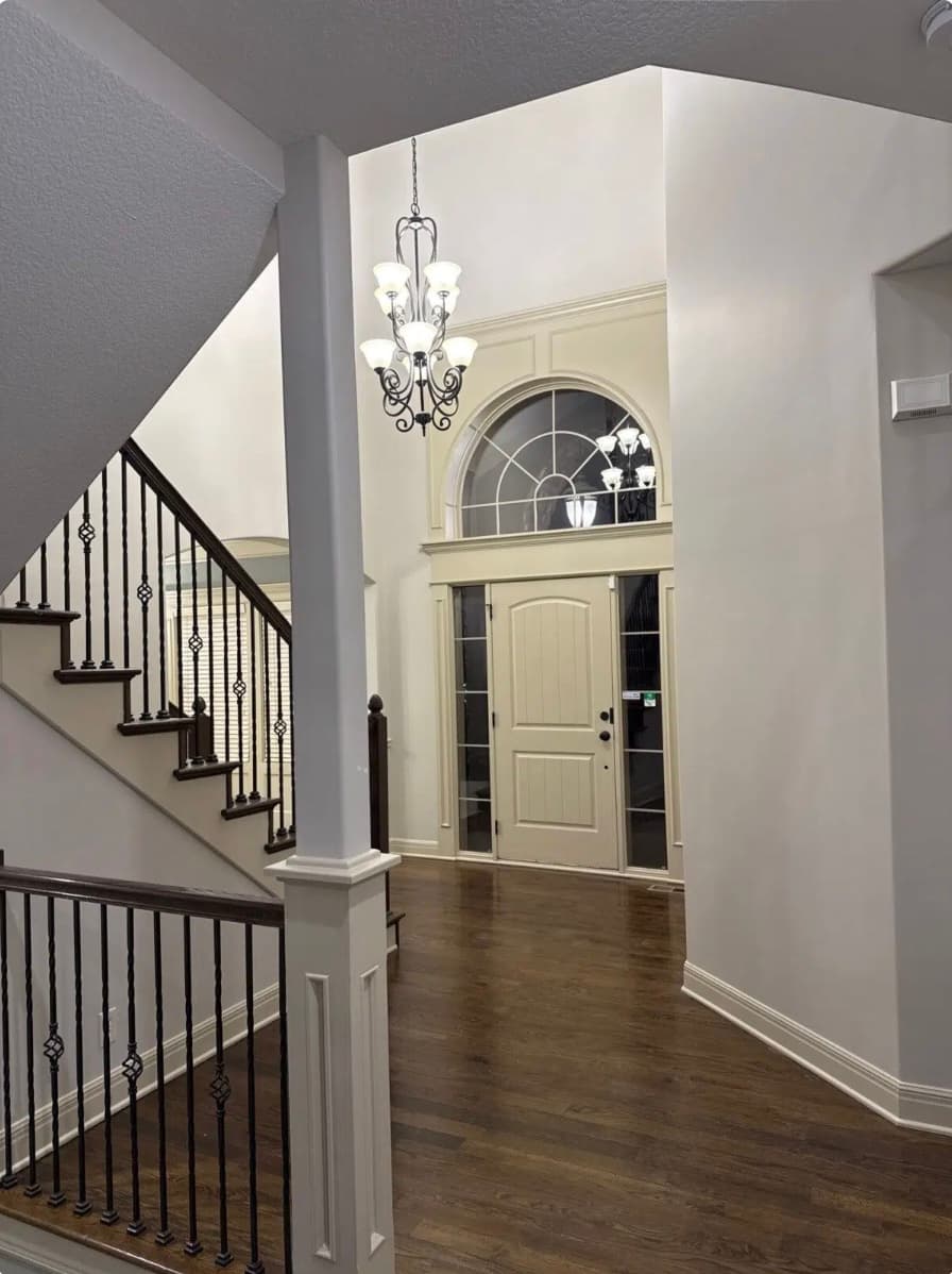Spacious home entryway with a front door, arched window, chandelier, and dark wood staircase.