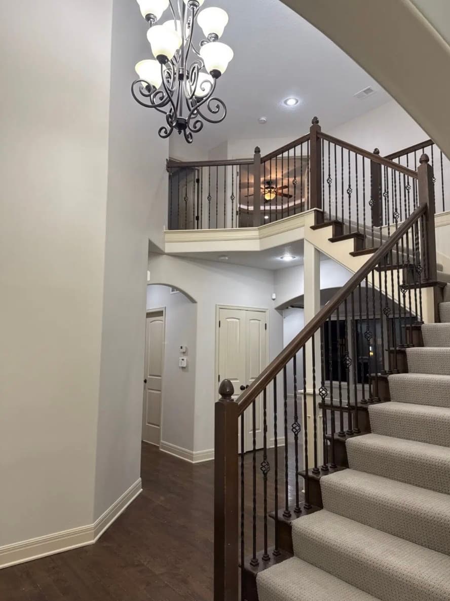 Two-story home foyer with a carpeted staircase, dark wood railings, and a hanging chandelier.
