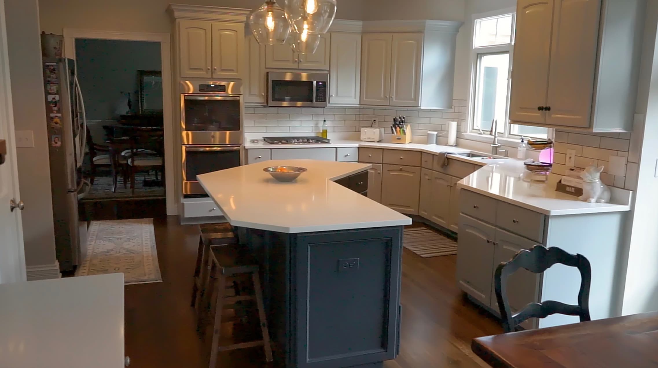 Modern kitchen with light grey cabinets, a dark island, white countertops, and stainless steel appliances.