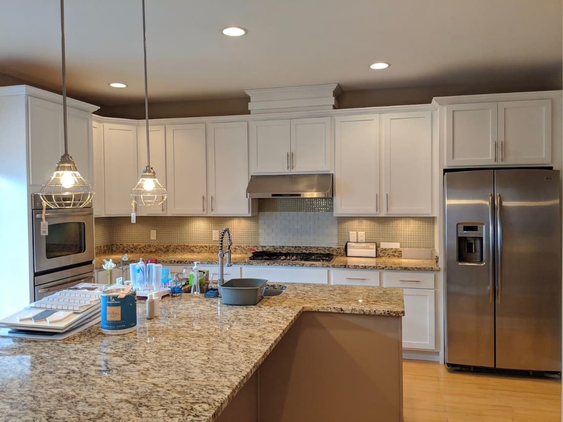 Modern kitchen featuring white cabinets, granite countertops, stainless steel appliances, and industrial pendant lights.