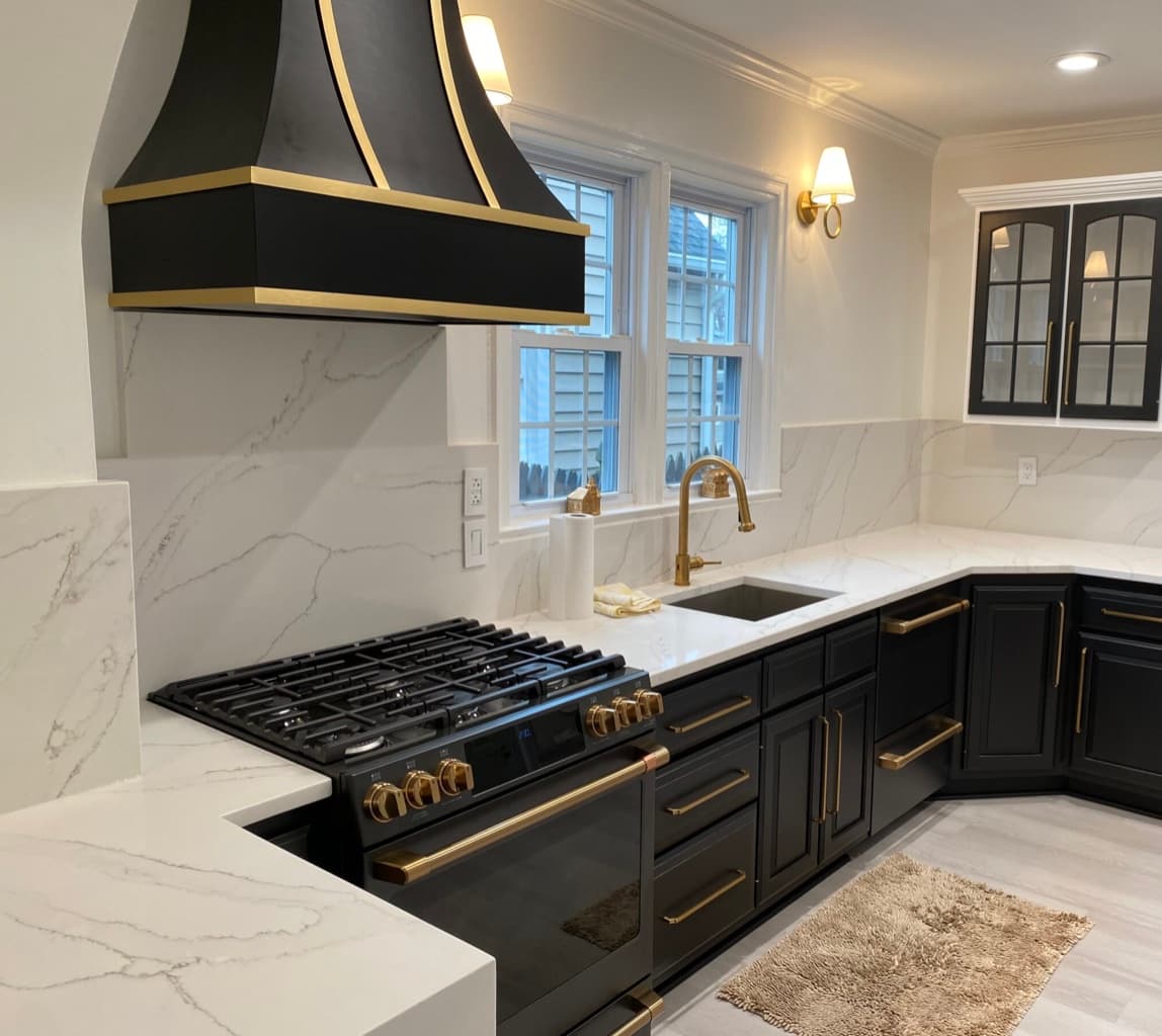 Modern kitchen with black cabinetry, white marble countertops, and elegant gold hardware and fixtures.