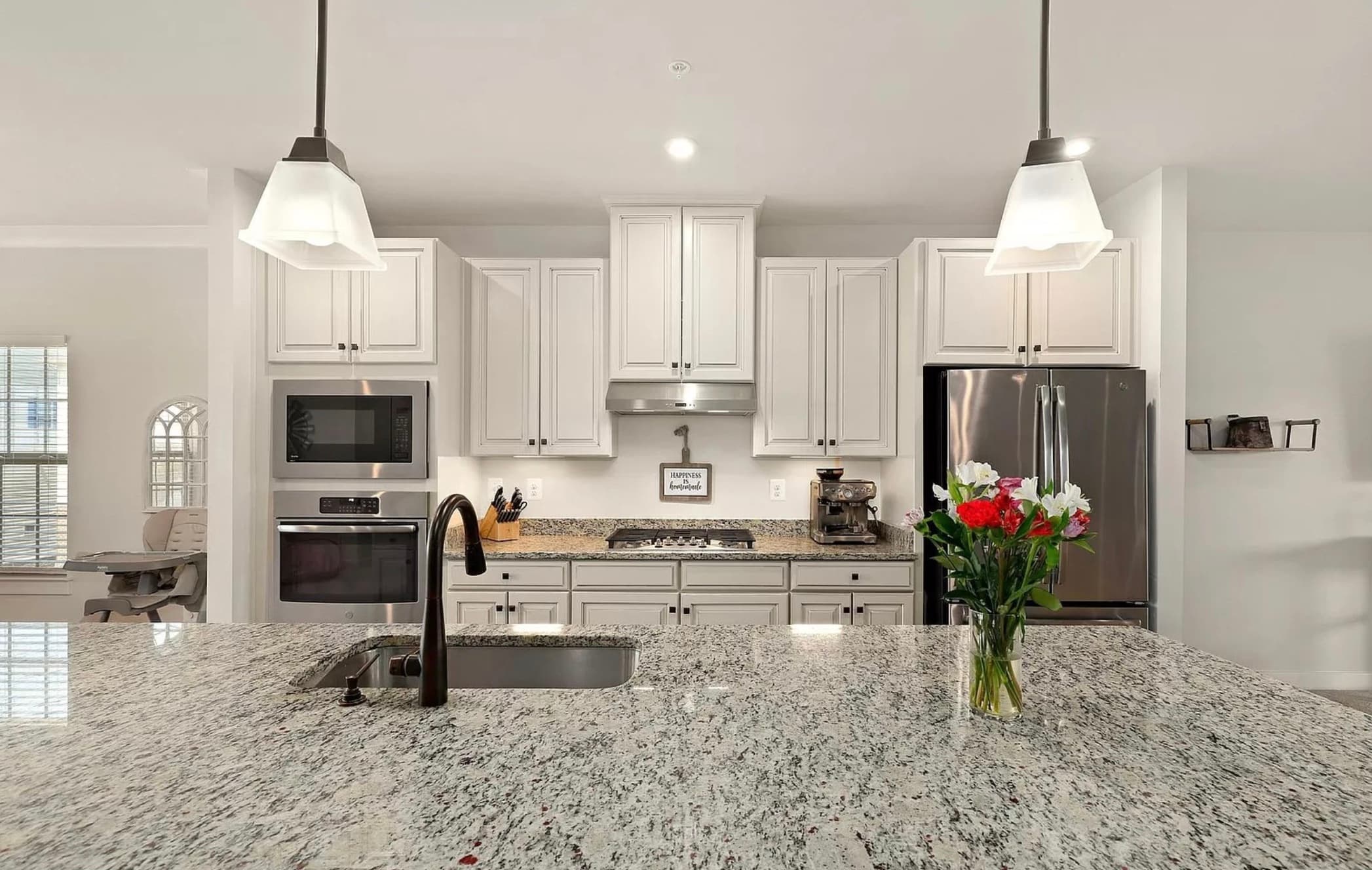 Modern kitchen with white cabinetry, granite countertops, stainless steel appliances, and a large central island.