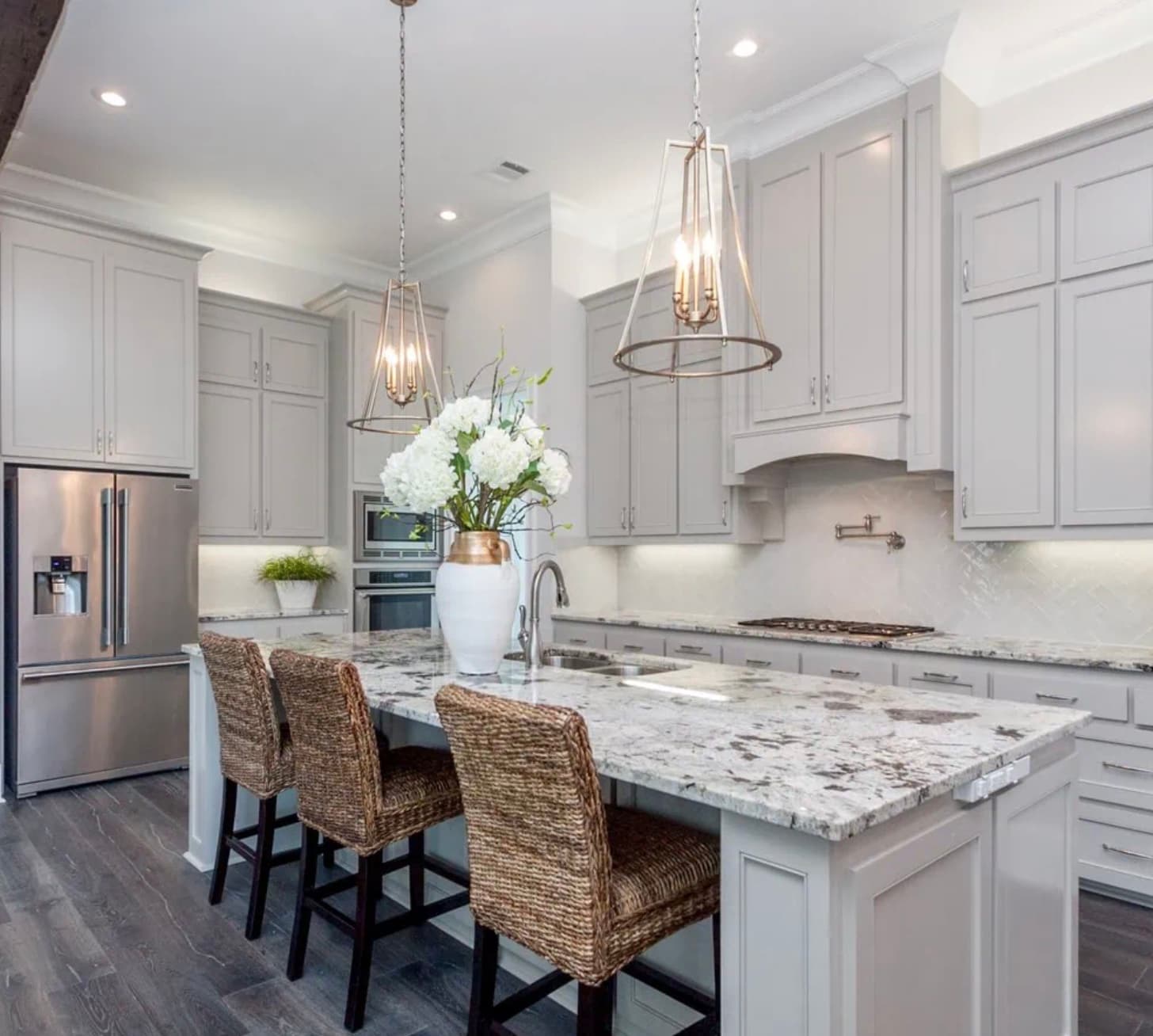 Modern kitchen featuring gray cabinets, granite island, woven bar stools, and elegant pendant light fixtures.