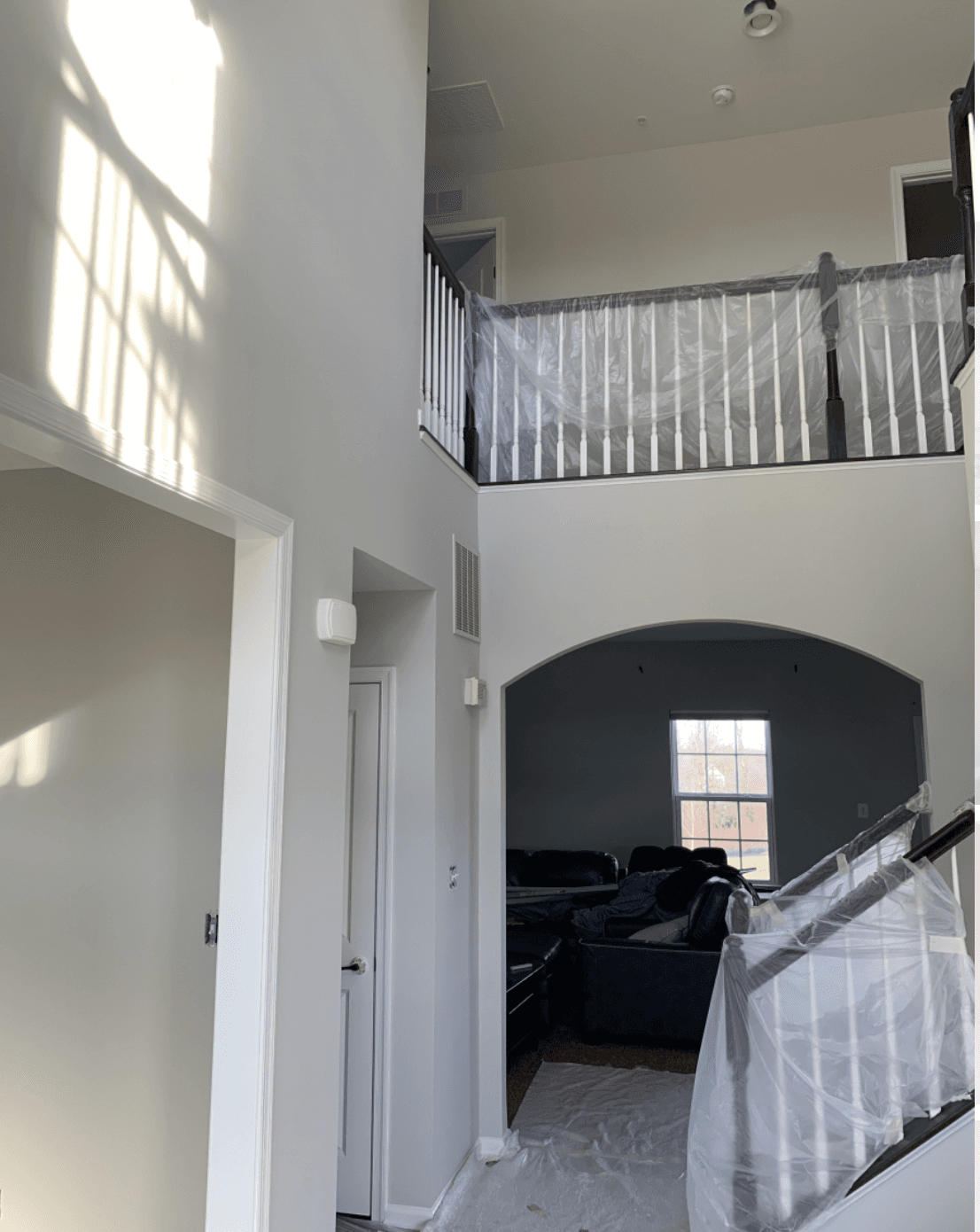 Sunlit interior of a two-story home with white walls and plastic-covered railings during renovation.